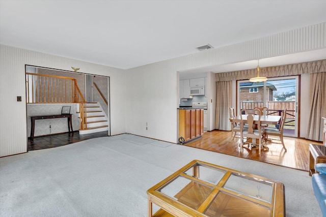 living area featuring light carpet, stairway, and visible vents