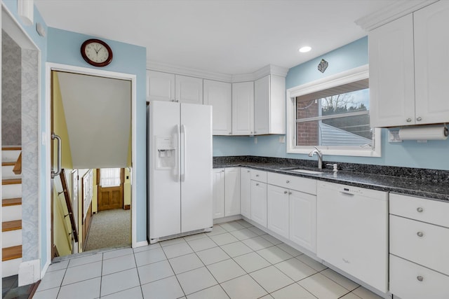 kitchen with light tile patterned floors, white appliances, a sink, white cabinetry, and dark stone countertops