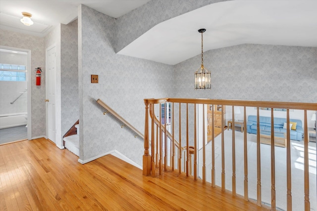 stairs with a chandelier, wood-type flooring, baseboards, and wallpapered walls