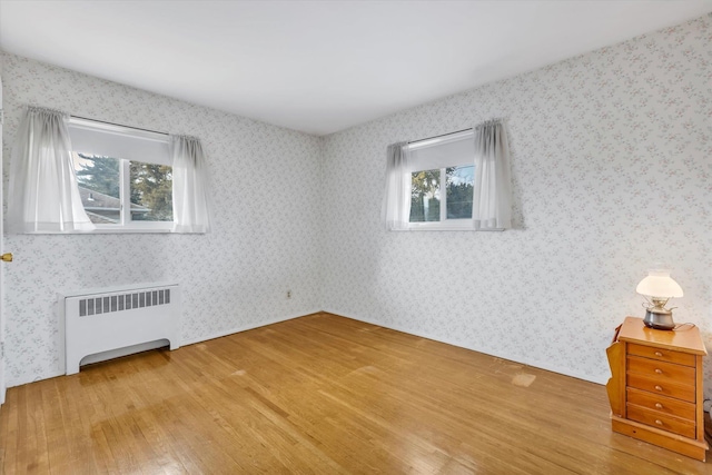 empty room featuring wood finished floors, radiator, and wallpapered walls