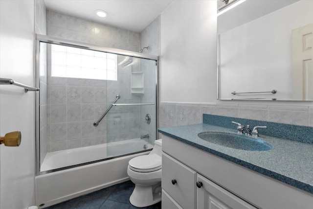 bathroom featuring toilet, shower / bath combination with glass door, tile patterned flooring, vanity, and tile walls