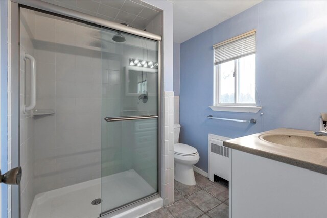 full bath with radiator heating unit, tile patterned flooring, a shower stall, and toilet