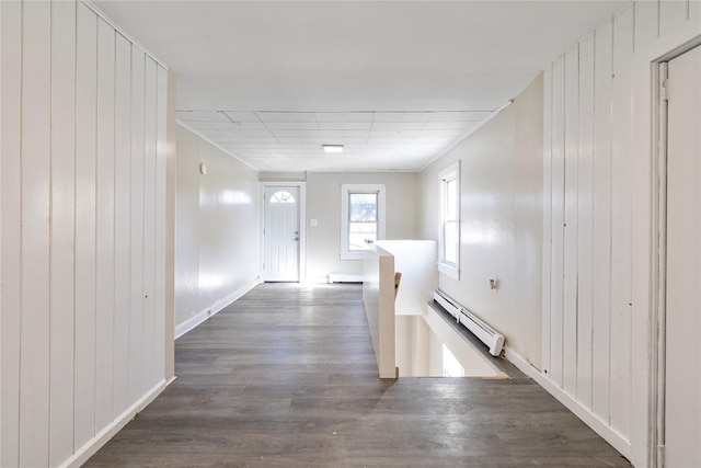 hallway with a baseboard heating unit, wood walls, dark wood finished floors, and an upstairs landing