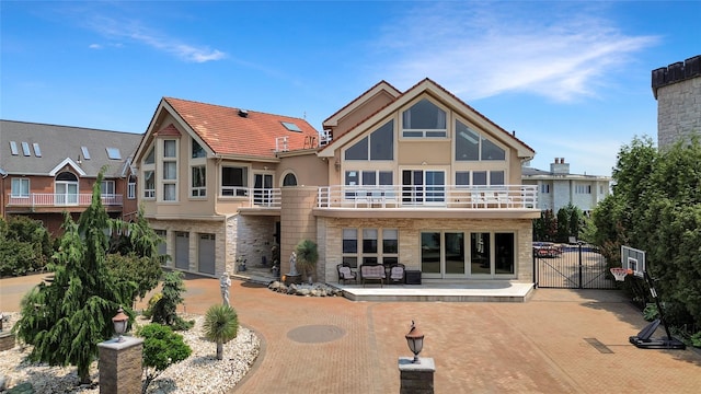 rear view of property with stucco siding, a gate, a patio area, a balcony, and stone siding