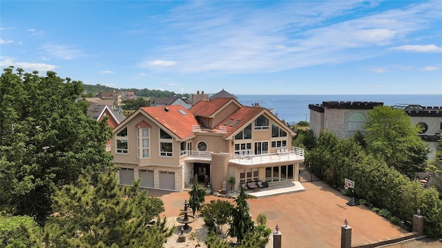 rear view of property featuring stone siding, an attached garage, a water view, and stucco siding