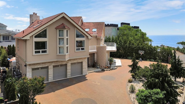 view of front facade with stone siding, a water view, a balcony, and stucco siding