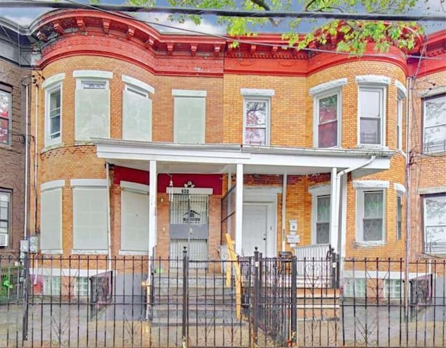 view of property with a fenced front yard, covered porch, and brick siding