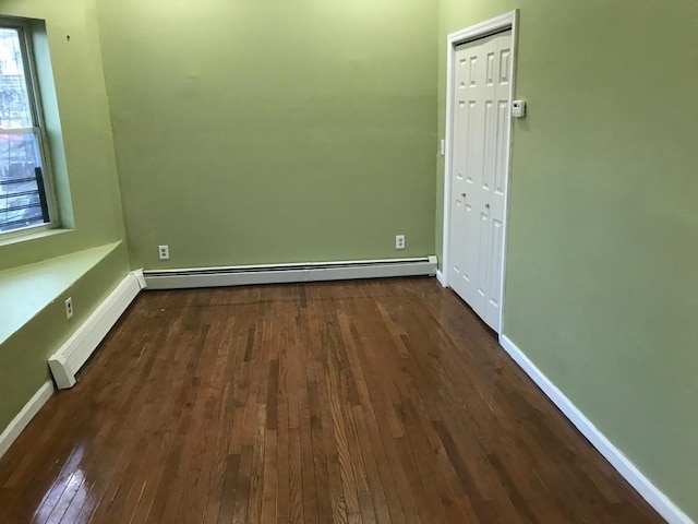 spare room with a baseboard heating unit, a baseboard radiator, dark wood-style floors, and baseboards