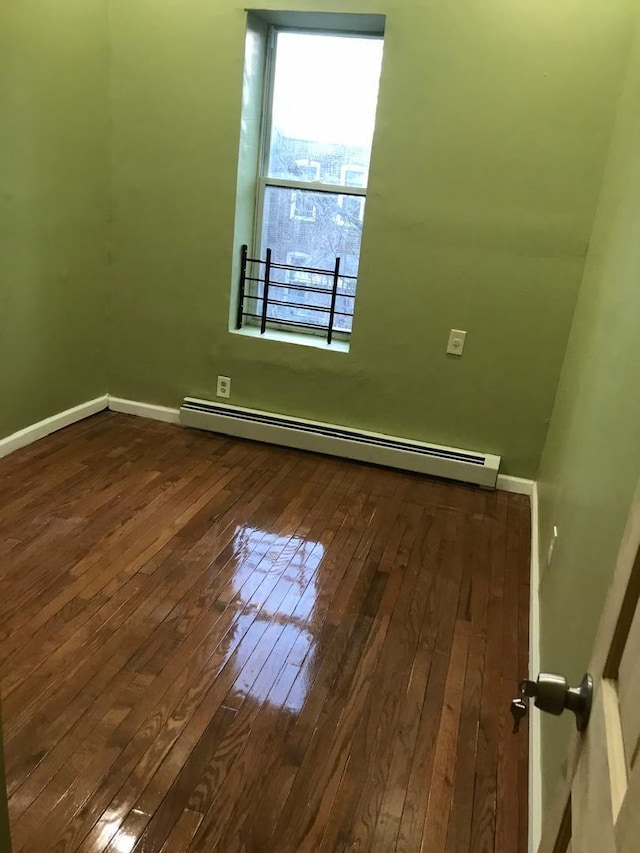 unfurnished room with a baseboard heating unit, baseboards, and hardwood / wood-style floors