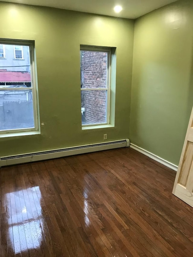 spare room featuring dark wood-type flooring, baseboard heating, and baseboards