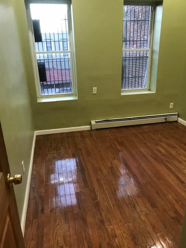 empty room featuring a baseboard radiator, baseboards, and hardwood / wood-style floors