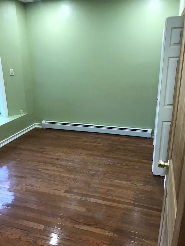 unfurnished room featuring baseboard heating and dark wood finished floors