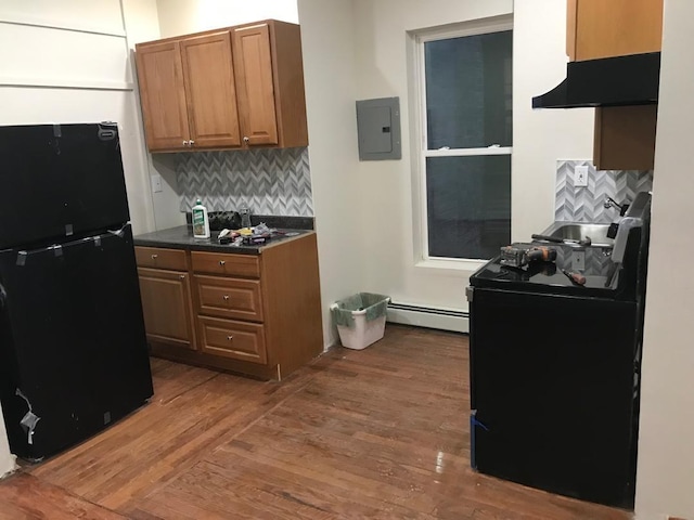 kitchen featuring wood finished floors, baseboard heating, freestanding refrigerator, electric panel, and dark countertops