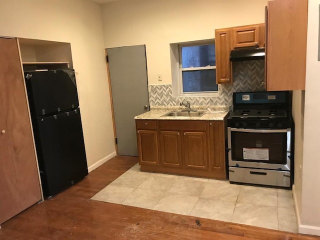 kitchen featuring under cabinet range hood, a sink, freestanding refrigerator, tasteful backsplash, and gas range