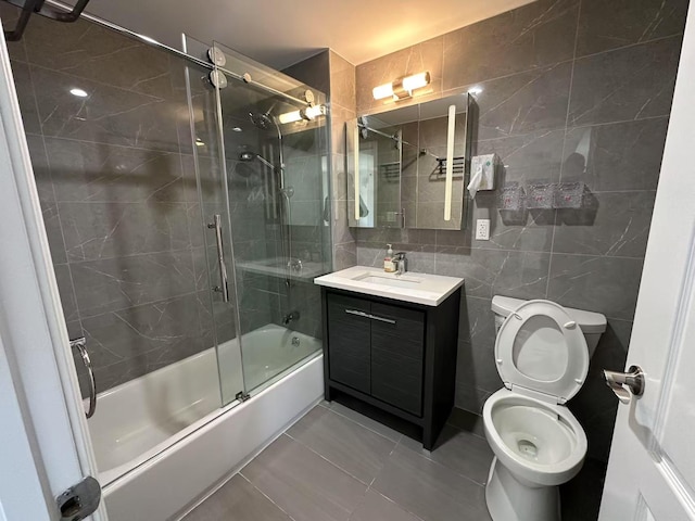 bathroom featuring tile patterned flooring, toilet, vanity, tile walls, and combined bath / shower with glass door