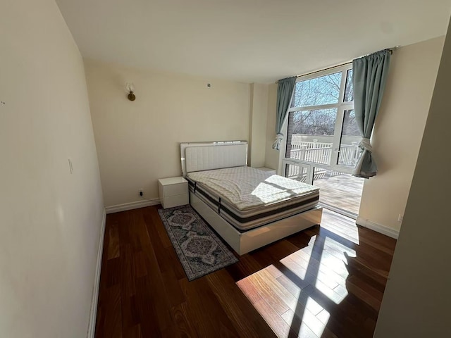 bedroom with access to exterior, floor to ceiling windows, baseboards, and wood finished floors