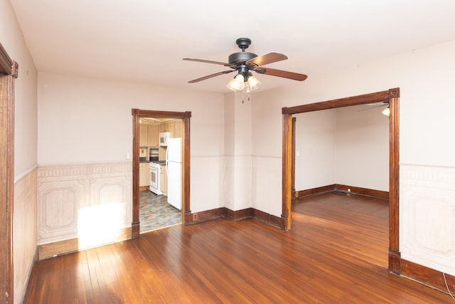 unfurnished room with dark wood finished floors, a ceiling fan, and baseboards