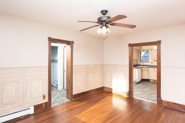 unfurnished room with a sink, a baseboard radiator, wood-type flooring, and a ceiling fan