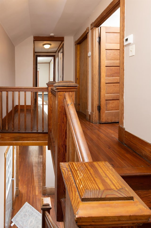 hall with an upstairs landing, lofted ceiling, baseboards, and wood finished floors