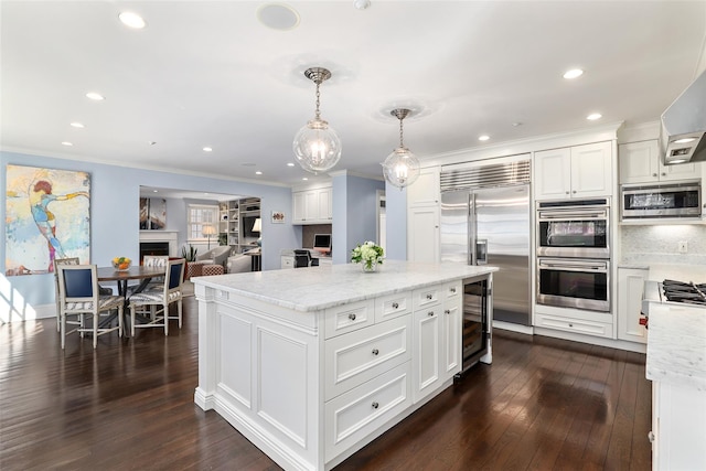 kitchen featuring stainless steel appliances, a fireplace, white cabinetry, dark wood finished floors, and crown molding