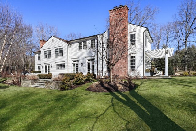 back of house featuring a patio area, a chimney, a lawn, and a pergola