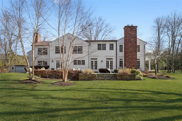 back of house featuring an outbuilding, a lawn, a chimney, and a patio