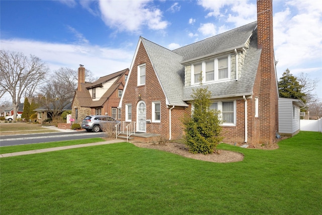 view of front of house featuring brick siding, a chimney, and a front yard