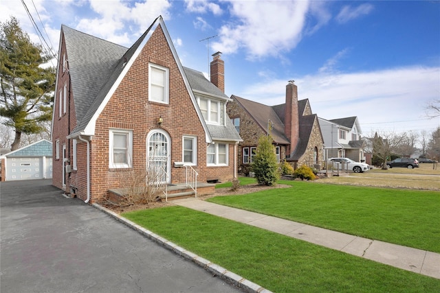 view of front of property with an outbuilding, brick siding, a detached garage, a chimney, and a front lawn