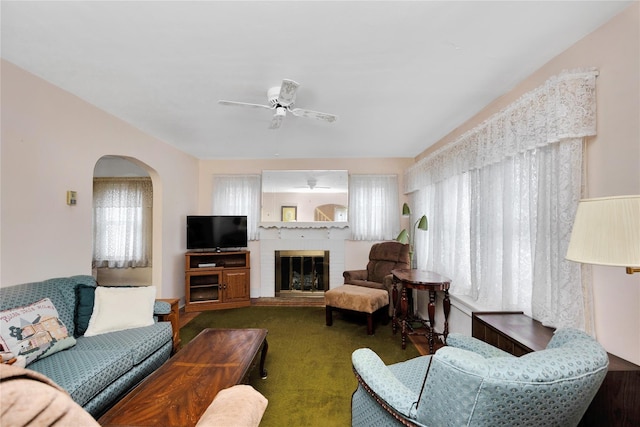 living area featuring a fireplace, arched walkways, and a ceiling fan