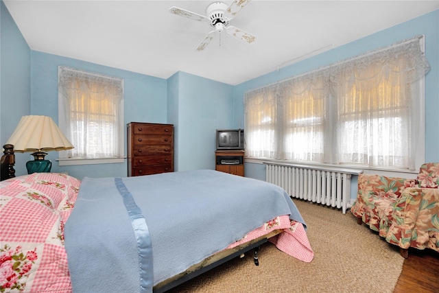 bedroom featuring a ceiling fan, multiple windows, and radiator heating unit