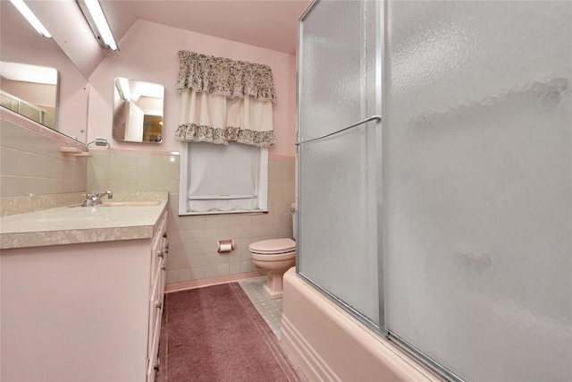 full bathroom with bath / shower combo with glass door, wainscoting, toilet, vanity, and tile walls