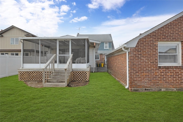 rear view of house featuring a yard, brick siding, fence, and a sunroom