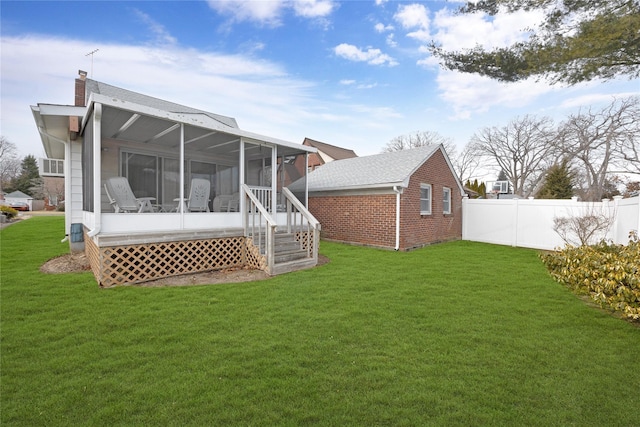 back of property featuring brick siding, fence, a sunroom, a lawn, and a chimney