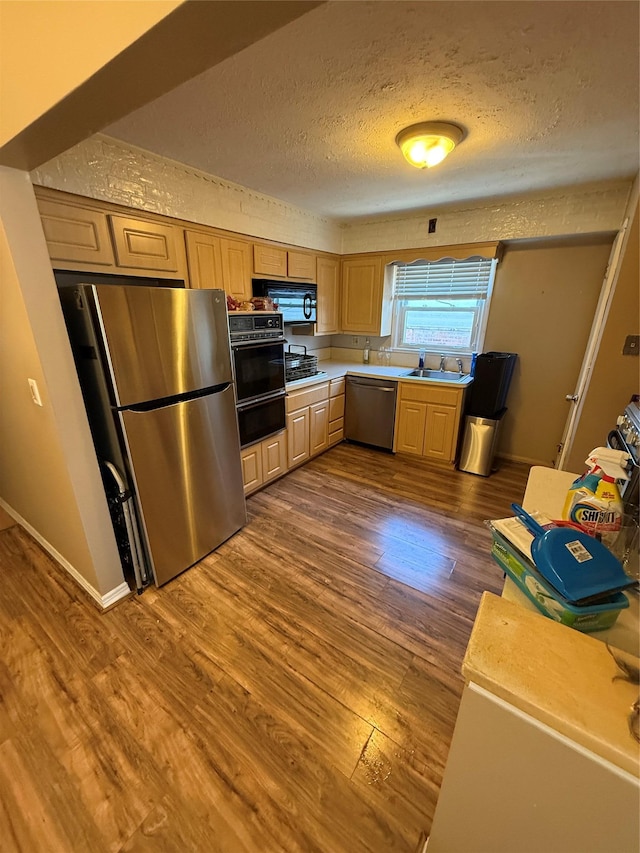 kitchen featuring a textured ceiling, a sink, light countertops, dark wood-style floors, and black appliances