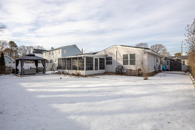 snow covered back of property with a sunroom, a gazebo, fence, an outdoor structure, and a shed