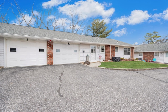 single story home featuring aphalt driveway, brick siding, a front lawn, and roof with shingles