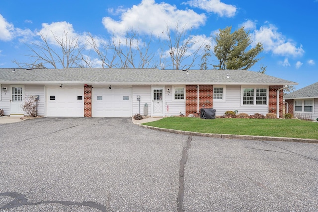 ranch-style home featuring roof with shingles, brick siding, a front yard, a garage, and driveway