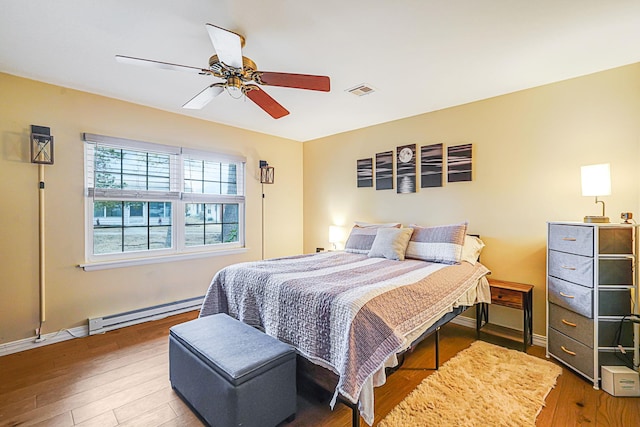 bedroom featuring visible vents, baseboard heating, a ceiling fan, wood finished floors, and baseboards