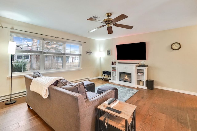 living area with baseboards, baseboard heating, hardwood / wood-style floors, and a glass covered fireplace