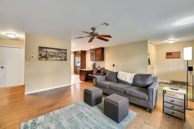 living area with light wood-style flooring, a ceiling fan, visible vents, and baseboards