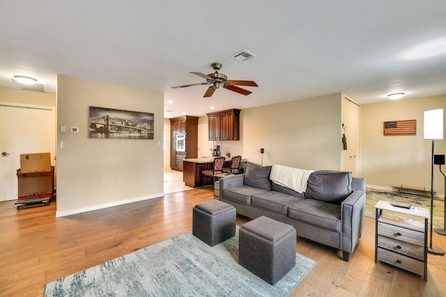 living area with a ceiling fan, baseboards, visible vents, and light wood finished floors