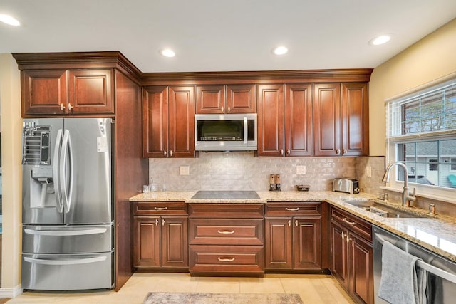 kitchen featuring appliances with stainless steel finishes, a sink, light stone counters, and tasteful backsplash