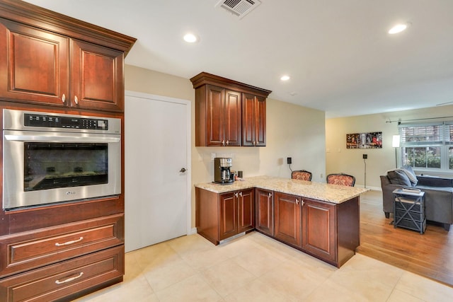 kitchen featuring visible vents, open floor plan, light stone countertops, oven, and a peninsula