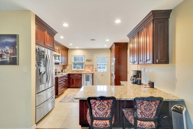 kitchen featuring light tile patterned floors, a peninsula, appliances with stainless steel finishes, light stone countertops, and tasteful backsplash