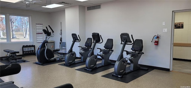 gym featuring a ceiling fan, baseboards, visible vents, and a drop ceiling