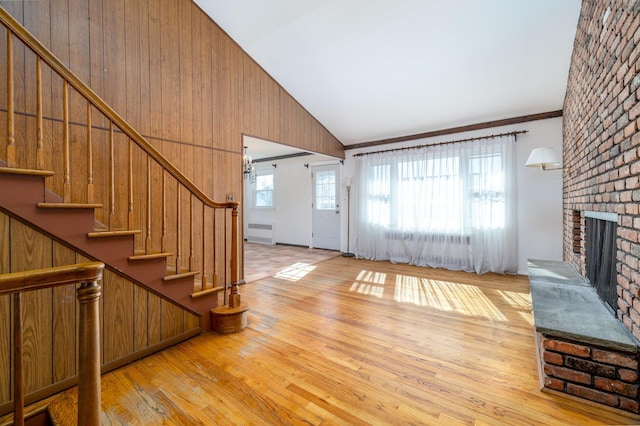 entrance foyer with high vaulted ceiling, wood finished floors, stairway, a brick fireplace, and radiator heating unit