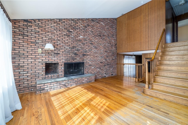 unfurnished living room featuring lofted ceiling, brick wall, wood finished floors, stairs, and a brick fireplace