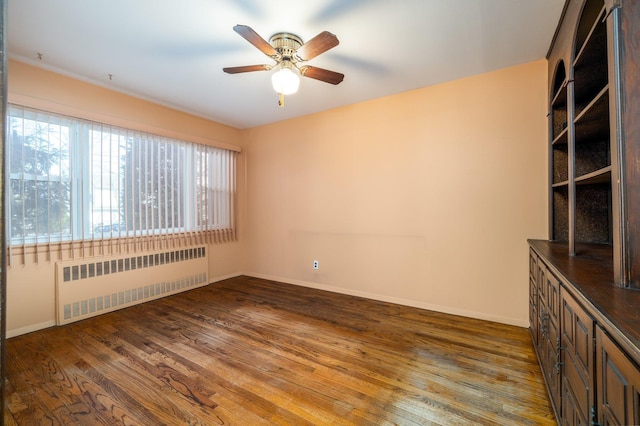 empty room with radiator, a ceiling fan, baseboards, and wood finished floors