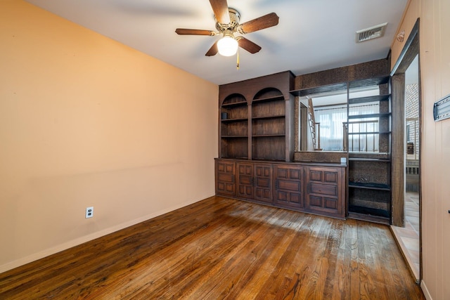 empty room with baseboards, visible vents, built in features, wood-type flooring, and ceiling fan