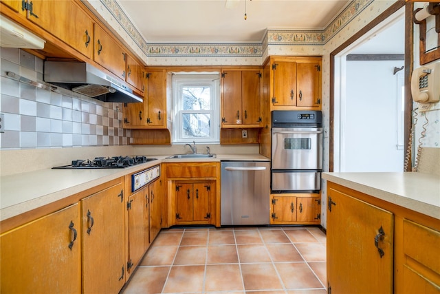 kitchen with under cabinet range hood, a sink, light countertops, appliances with stainless steel finishes, and a warming drawer